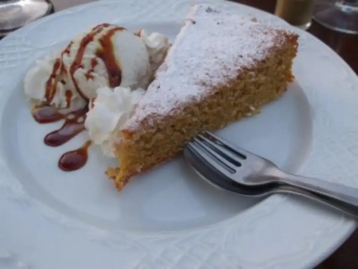 Ein St&uuml;ck mallorquinischer Mandelkuchen mit Puderzucker, serviert mit Eis und Karamellsauce.