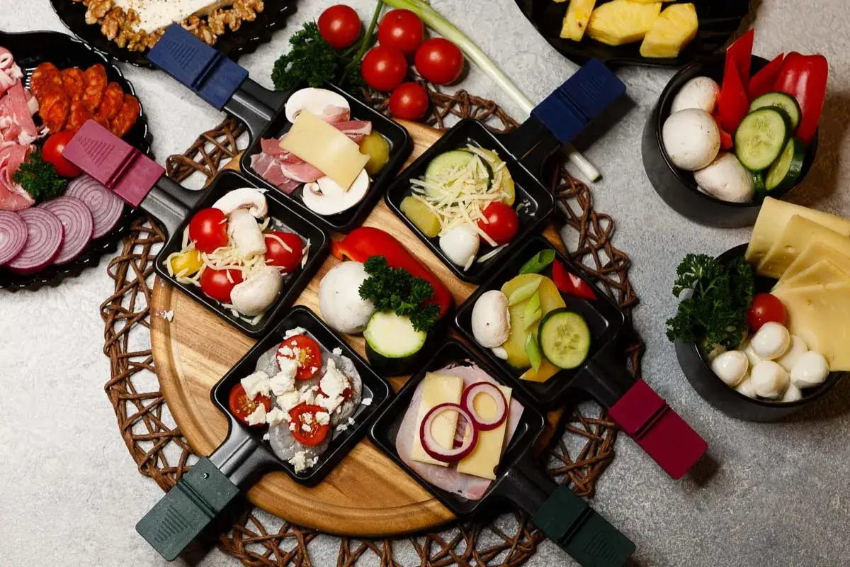 Raclette-Pf&auml;nnchen mit Pilzen, Tomaten, K&auml;se, Schinken, Zwiebeln, Garnelen und Gem&uuml;se. Hier sieht man, was kann man zu Raclette essen.