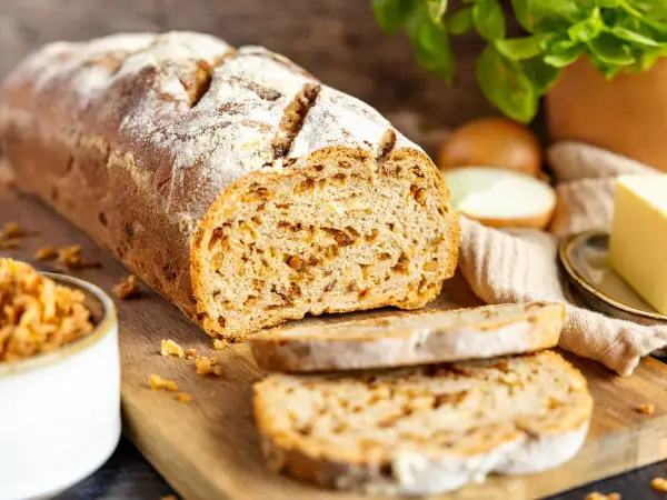 Frisch gebackenes Zwiebelbrot mit knusprigen Röstzwiebeln, bereit für ein köstliches Zwiebelbrot Rezept. Daneben Butter und frische Kräuter.