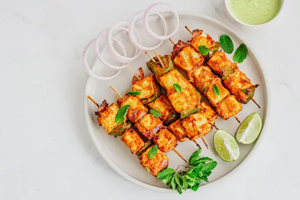 Saftiges paneer tikka auf Spießen, garniert mit Minze, Zwiebelringen und Limettenspalten.