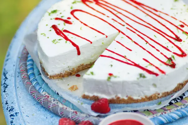 Cremiger Kuchen ohne Backen, dekoriert mit rotem Sirup und Limettenabrieb. Ein Stück ist bereits angeschnitten.