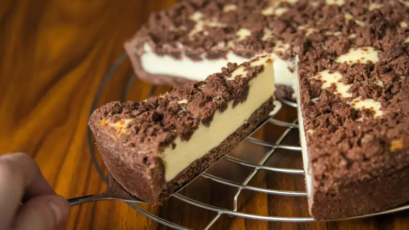 Ein Stück russischer Zupfkuchen wird aus dem Ganzen gehoben. Der Kuchen hat einen dunklen Boden, eine helle Füllung und eine krümelige Schokoladenstreusel-Decke.